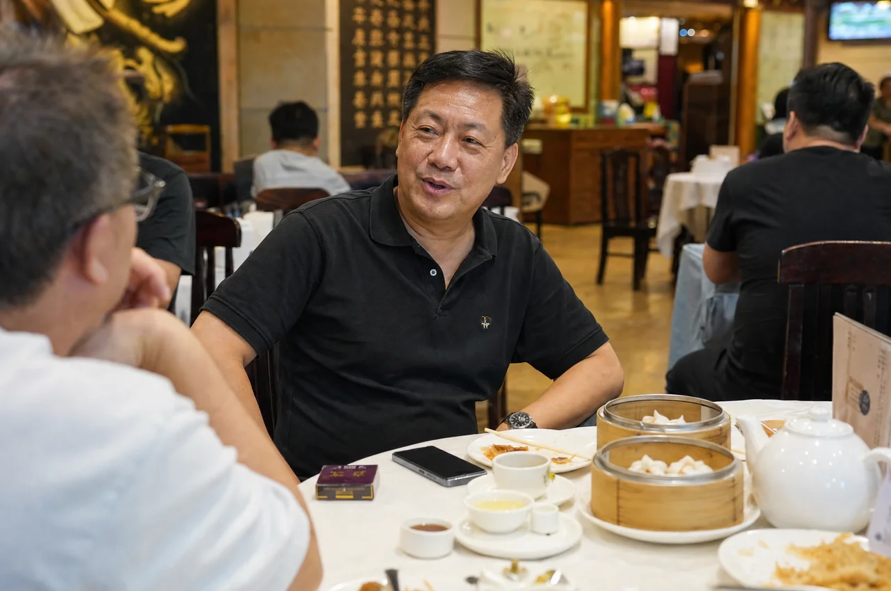 A landlord at a yum cha table in Hong Kong, mid-conversation, phone face-down beside the tea.